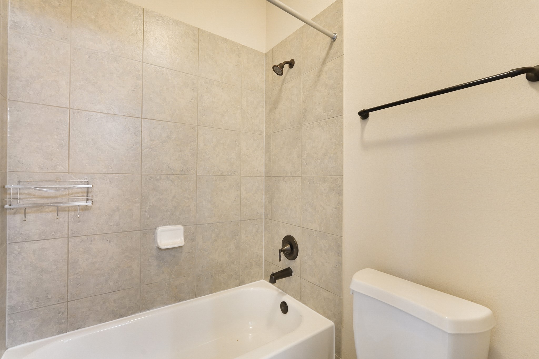 SECOND Flr-Bath#4: This bathroom features a tiled shower and tub combo with a modern showerhead and fixtures. It includes a wall-mounted towel bar and a simple toilet, offering a clean and functional space.