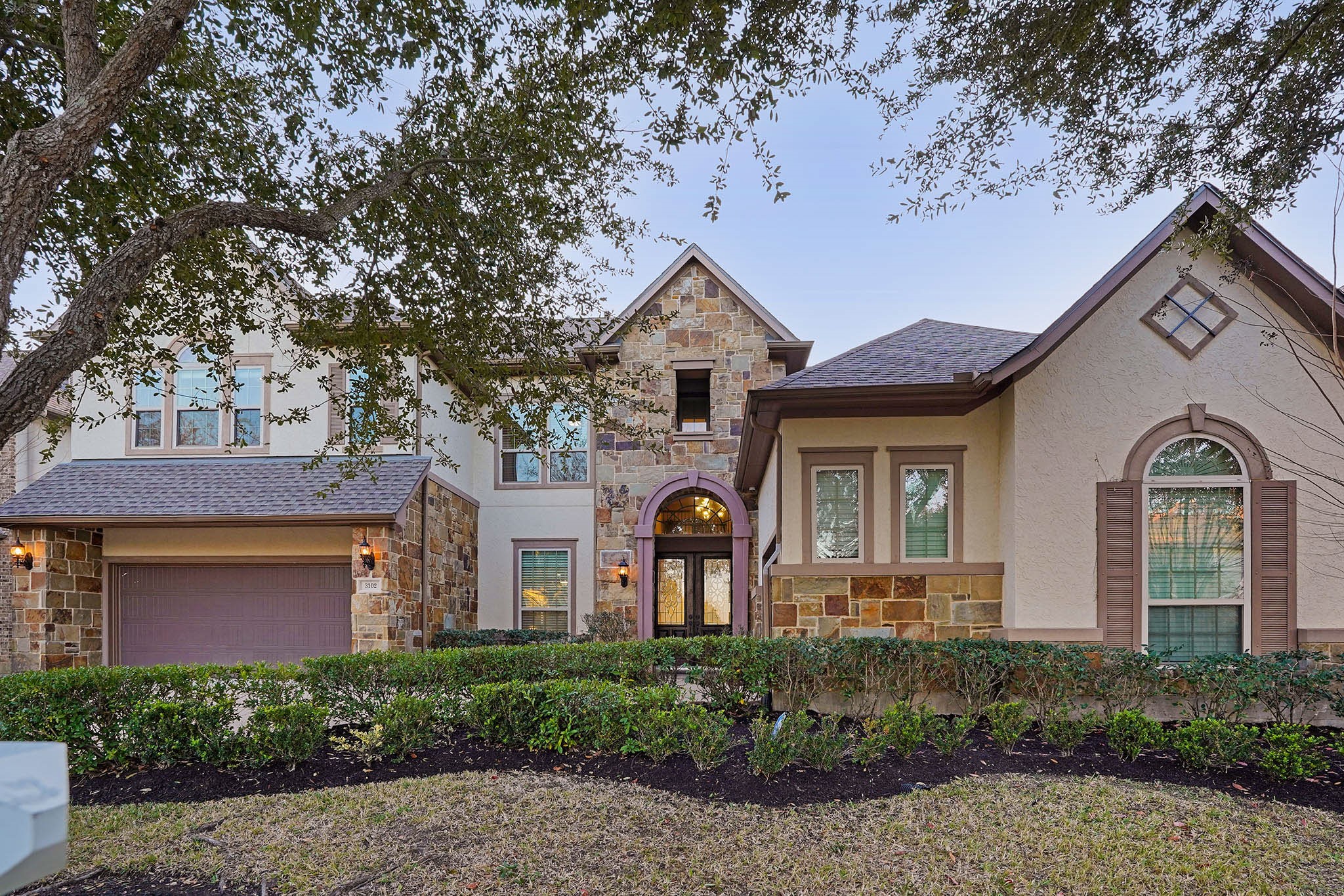 This elegant two-story, 5br-4.5ba home features a stone & stucco exterior, with a welcoming arched entryway and well-maintained landscaping. The attached 3-car garage and large windows enhance its curb appeal, nestled under mature trees.
