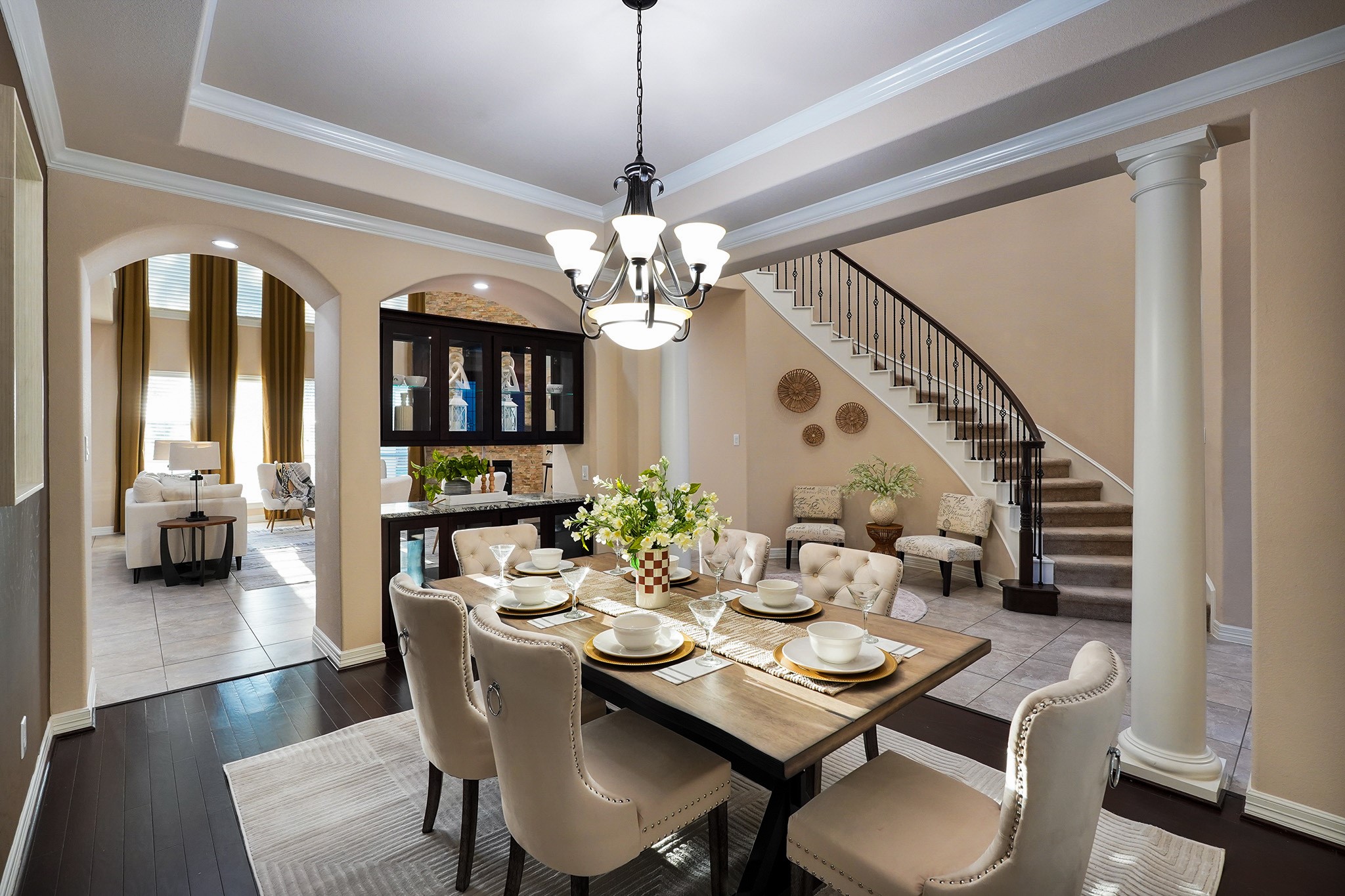 This elegant dining area features a stylish chandelier, coffered ceiling, and a warm accent wall. It opens to a bright living space with tall windows and high ceilings, offering a sophisticated and inviting atmosphere.