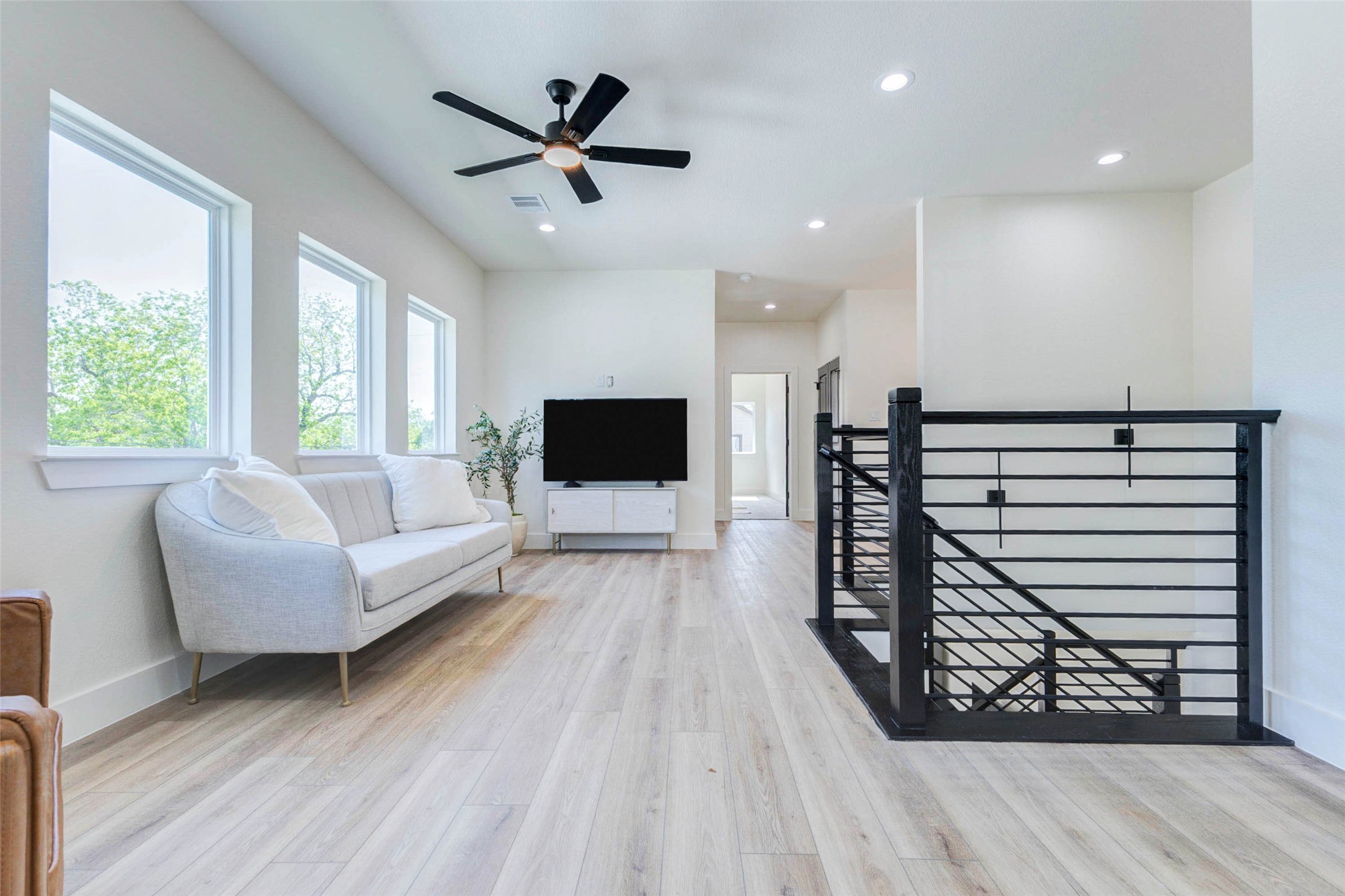 Recessed LED lighting and a contemporary ceiling fan complement the airy feel of the upper-floor gallery. Four oversized picture windows line the wall, flooding the second-story flex space with natural light.