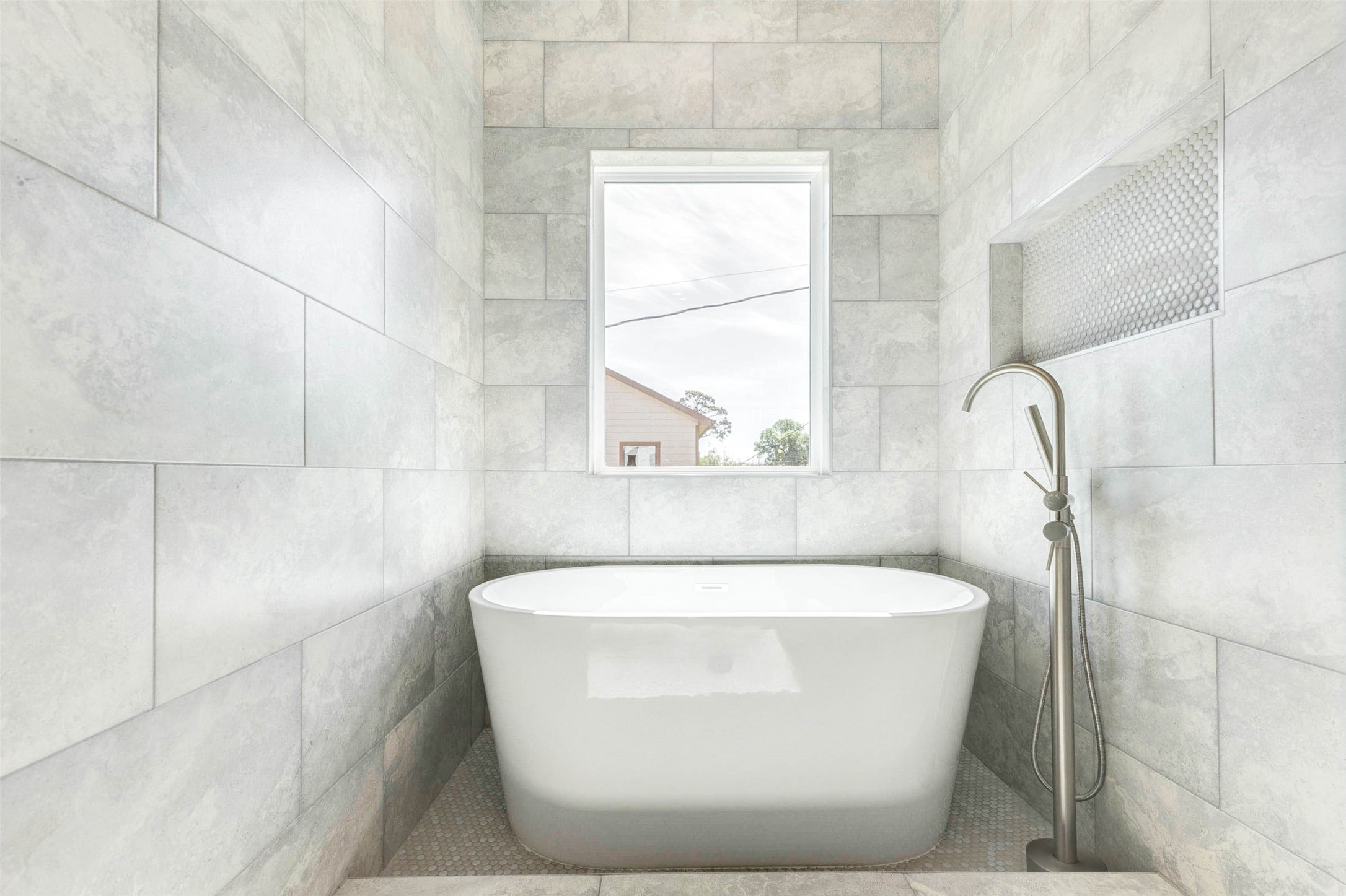 A freestanding soaking tub is centered beneath a large privacy window within a fully tiled wet area.