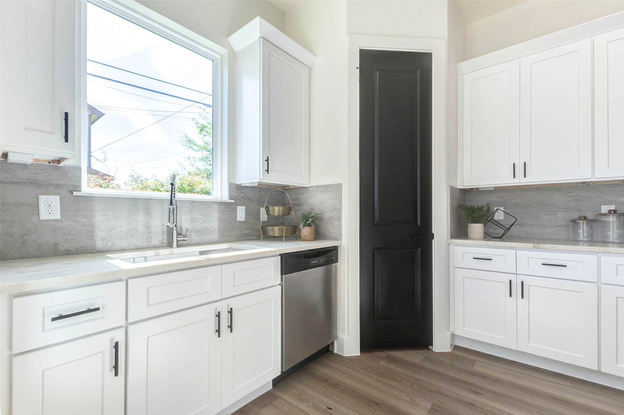The functional kitchen design includes a deep basin sink, integrated dishwasher, and a contrasting black pantry door.