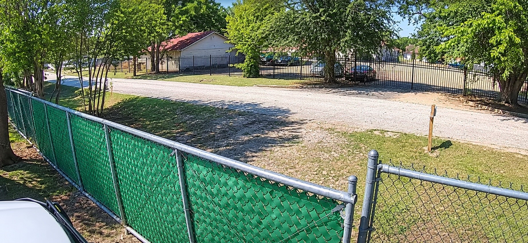 Gated and fenced property featuring a gravel driveway, mature trees, and open space.