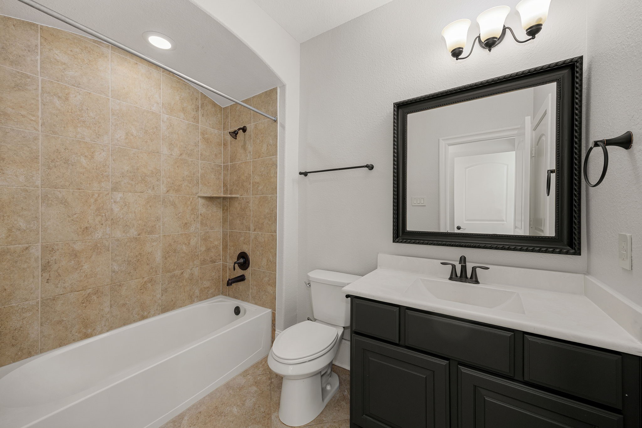 This secondary bathroom offers a tub/shower combo framed in warm tile, complemented by an elegant vanity and designer lighting.