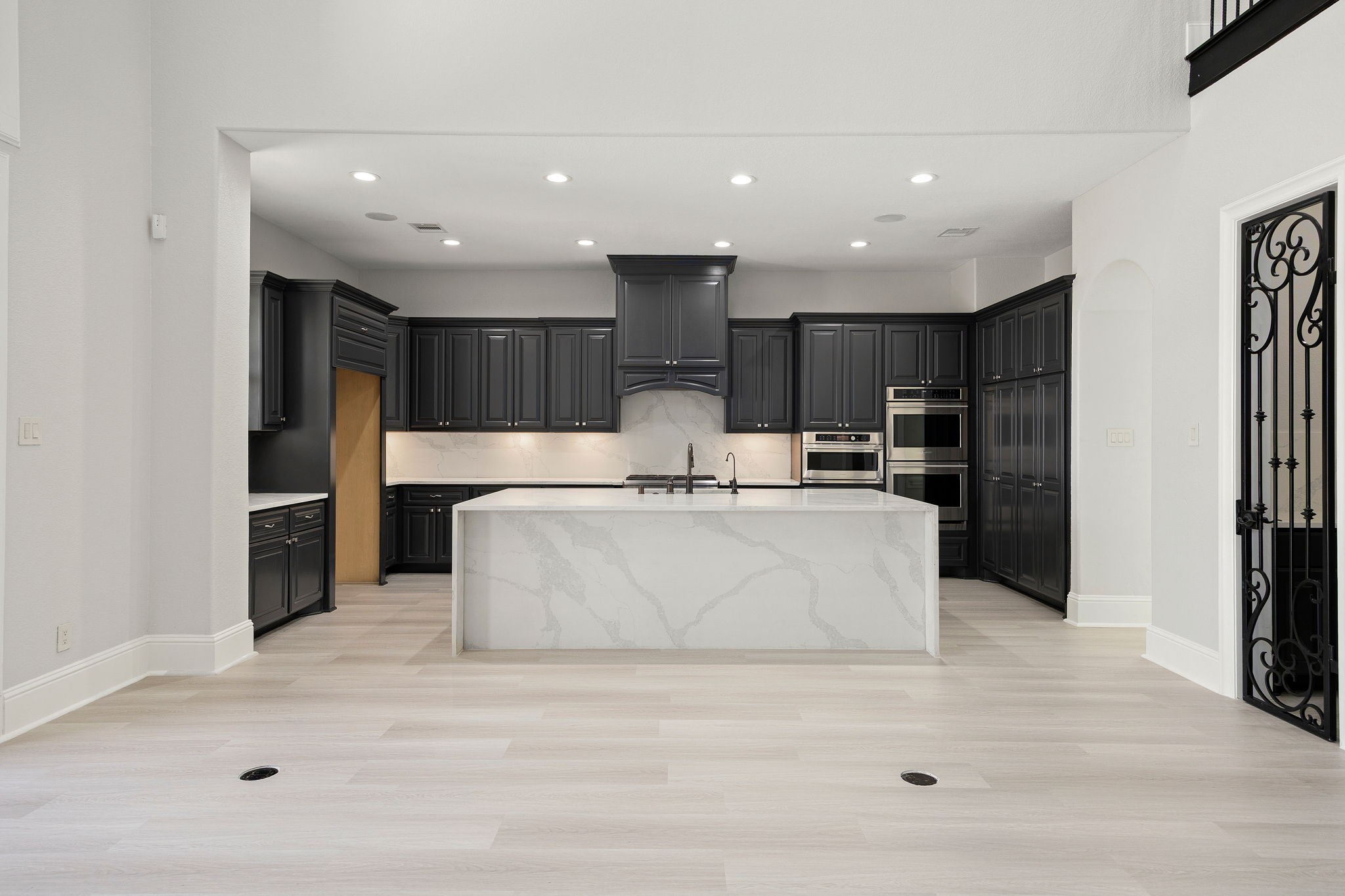 This impressive kitchen features a large island with breakfast bar seating, sleek dark cabinetry, double ovens, and recessed lighting throughout.