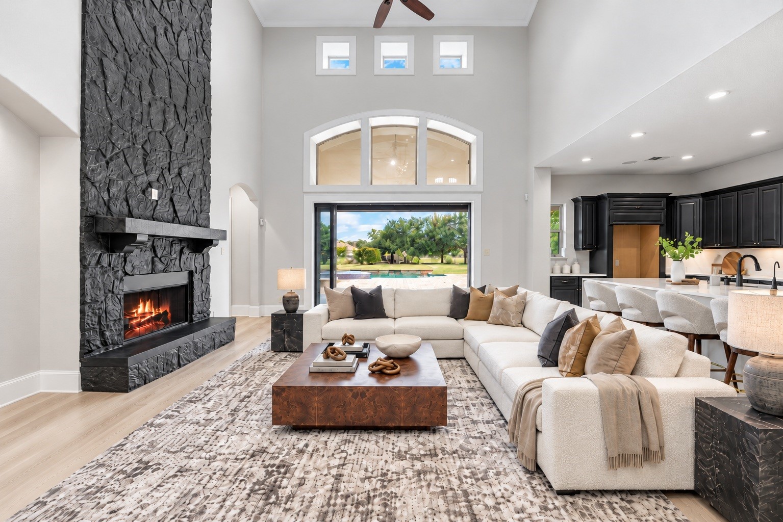 The living area impresses with a dramatic two-story stone fireplace and oversized windows, opening seamlessly to the backyard through sliding glass doors. Virtually staged. The living area impresses with a dramatic two-story stone fireplace and oversized windows, opening seamlessly to the backyard through sliding glass doors. Virtually staged.
