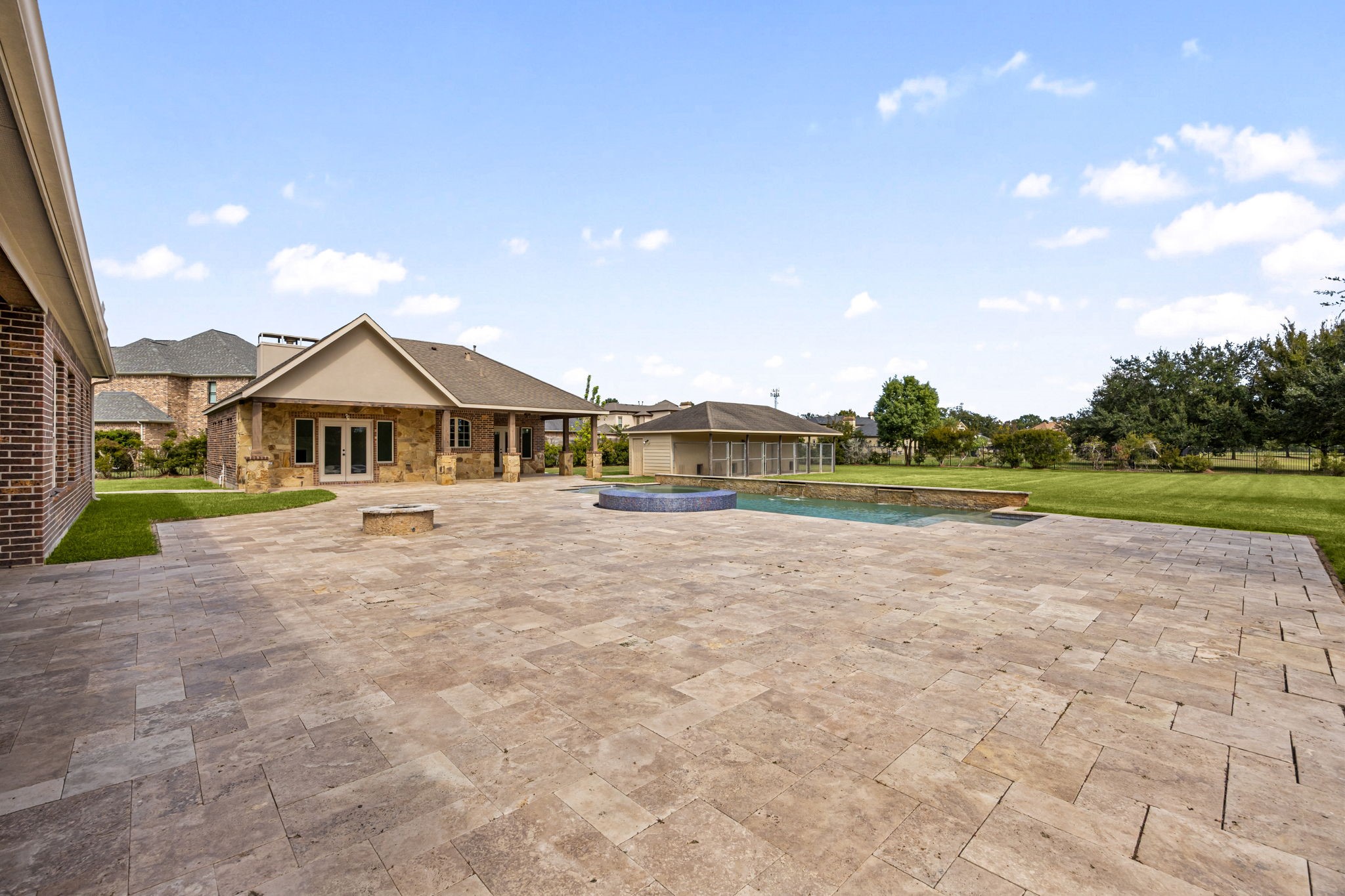 The expansive backyard unfolds across the propertys acre-plus lot, anchored by a sprawling travertine patio, a stone firepit, and the sparkling pool beyond, an entertainers paradise from every angle.