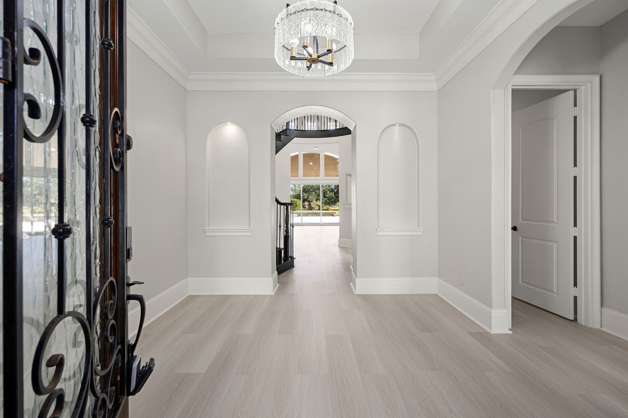 A dramatic wrought-iron front door opens into a grand foyer with soaring ceilings, a statement chandelier, and new flooring that flows throughout the home. A dramatic wrought-iron front door opens into a grand foyer with soaring ceilings, a statement chandelier, and new flooring that flows throughout the home.