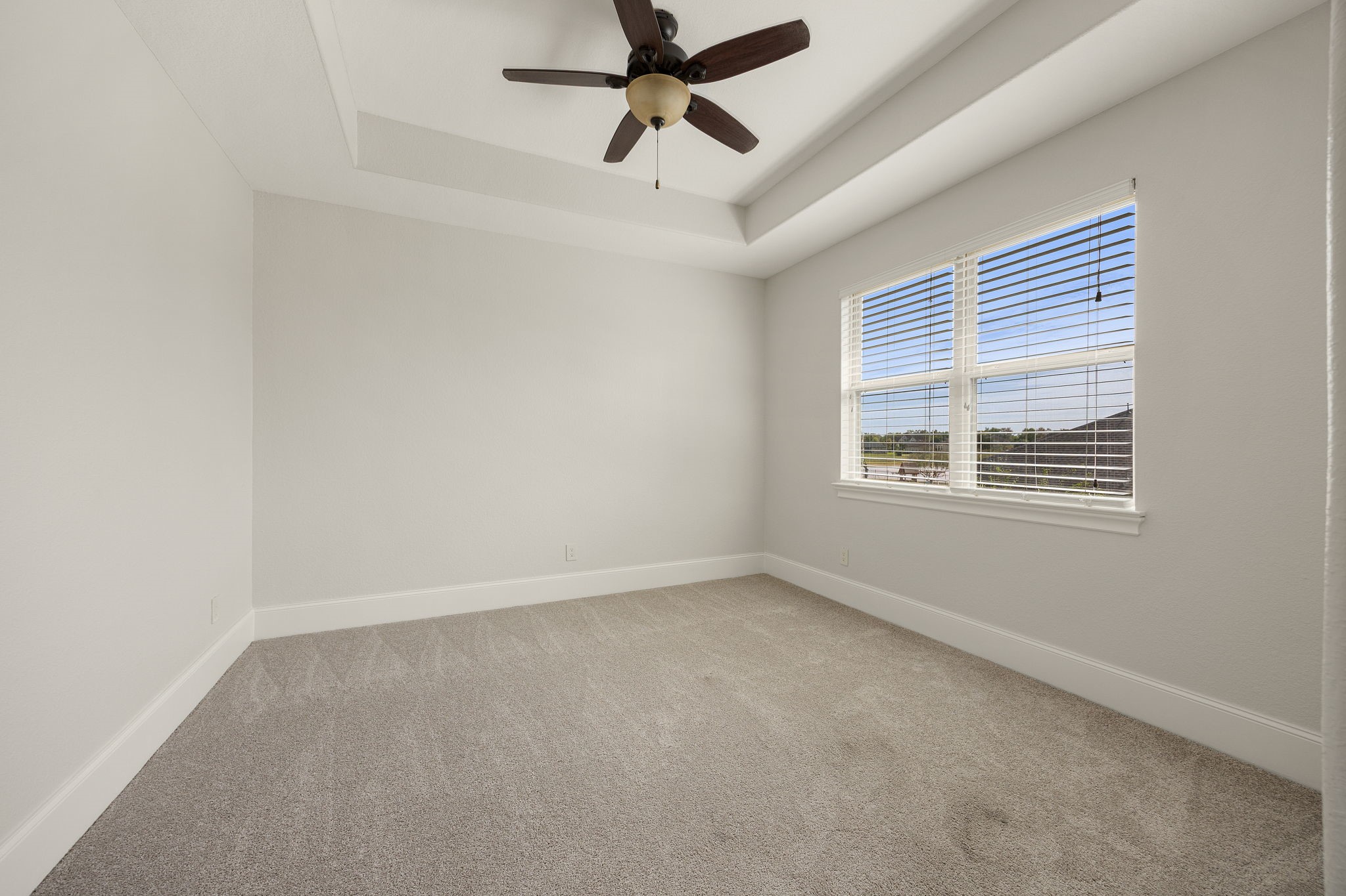 A beautifully proportioned secondary bedroom features a tray ceiling, ceiling fan, and generous windows overlooking the grounds below.