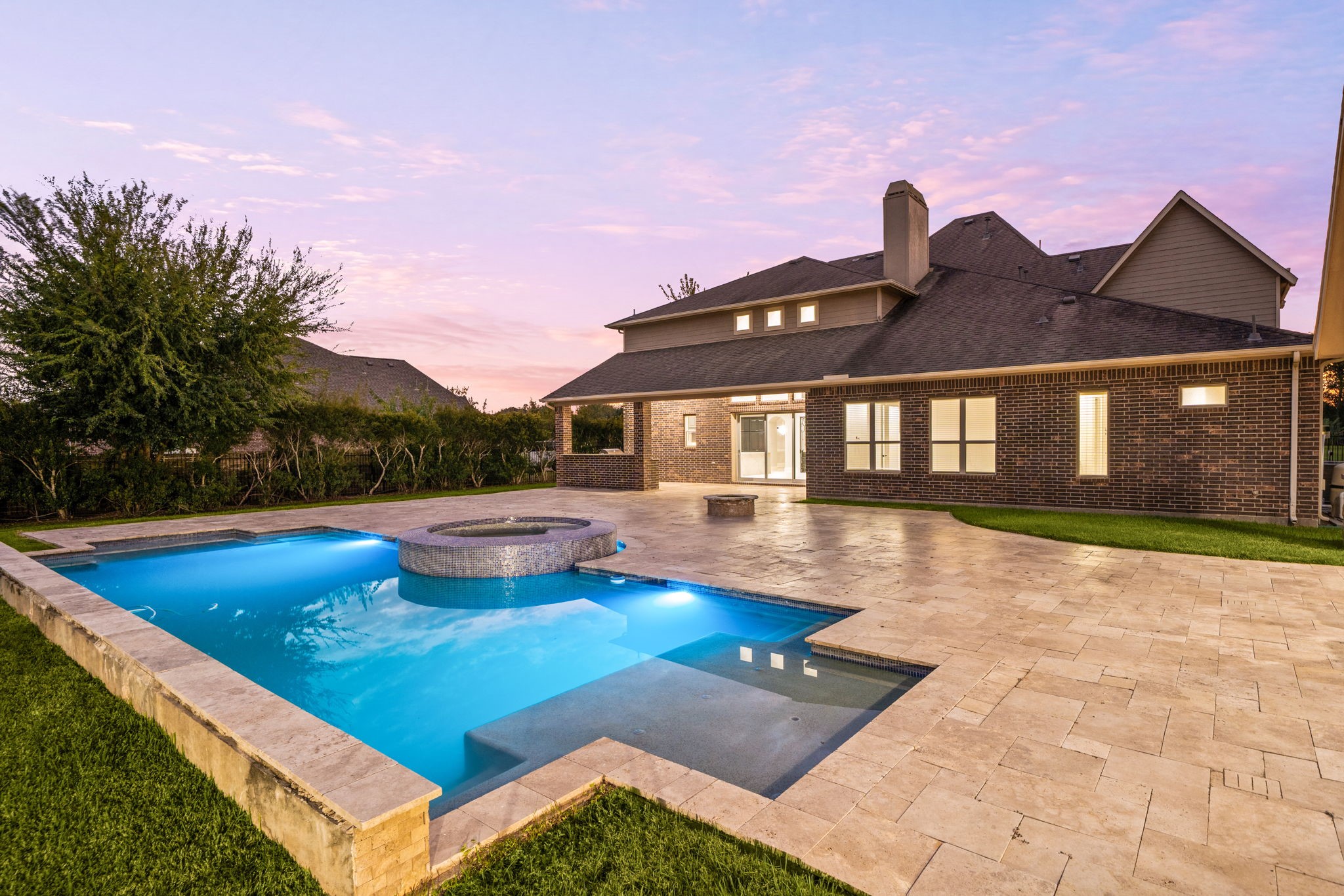 As evening falls, the pool and spa glow beautifully against the illuminated home, creating a resort-like ambiance perfect for entertaining.
