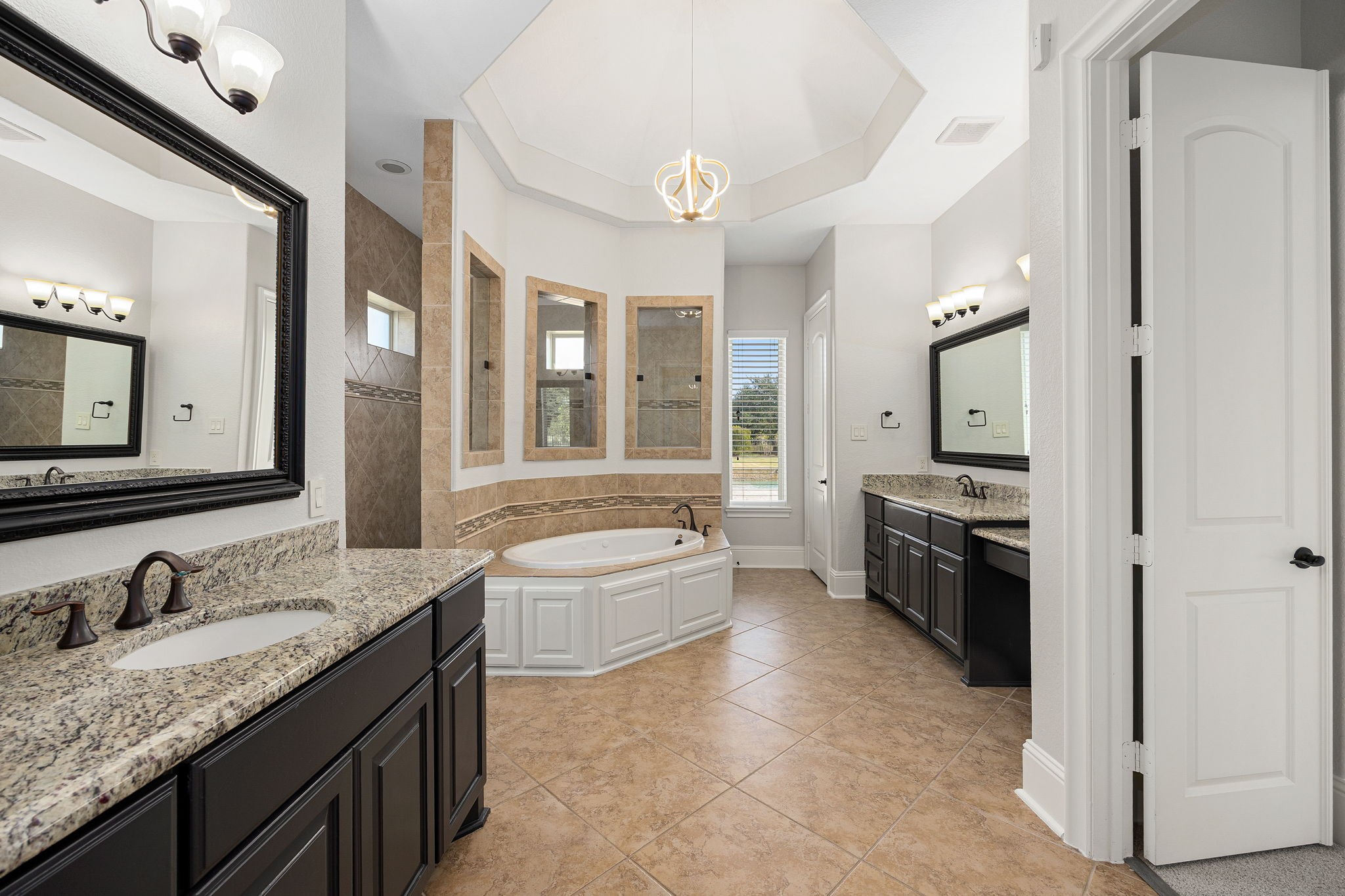 A true spa retreat, the ensuite is crowned by an elegant tray ceiling and crystal chandelier, with dual vanities and a corner soaking tub framed in custom tile.