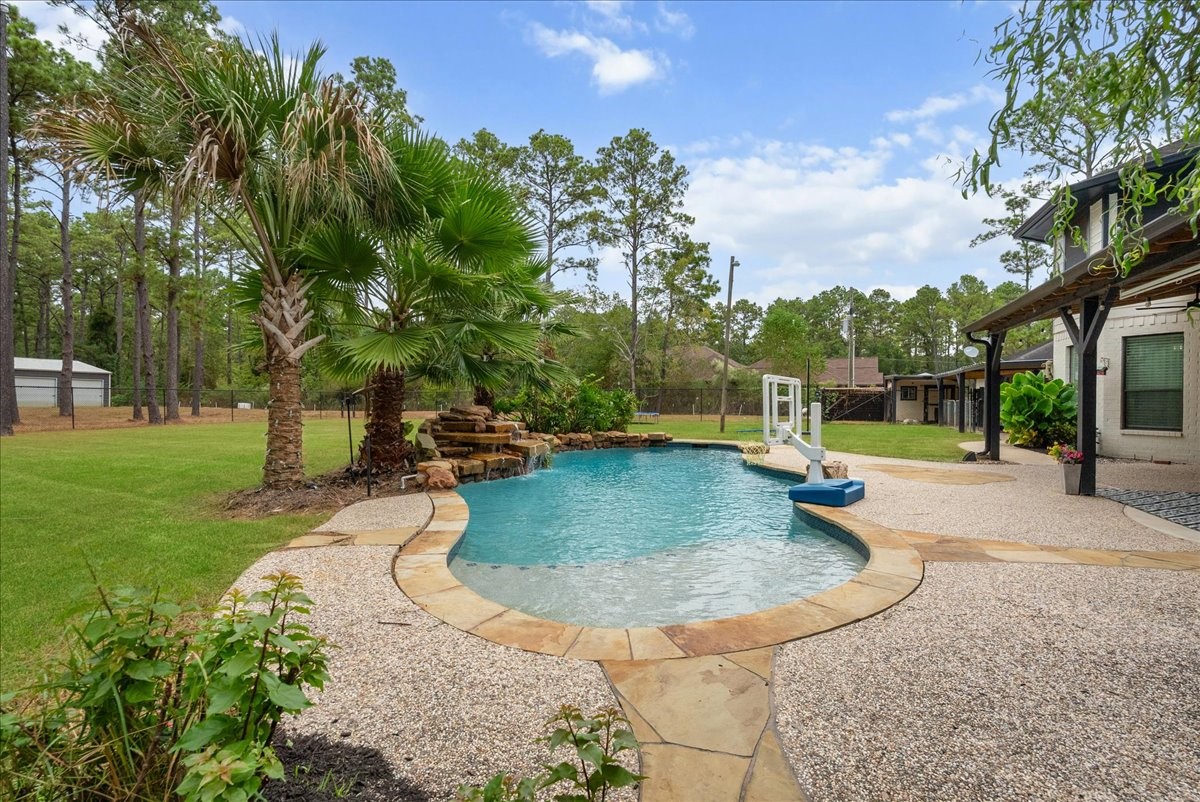 Experience serene outdoor living with a sparkling pool and waterfall feature, surrounded by lush landscaping and mature trees, perfect for relaxation and entertaining.