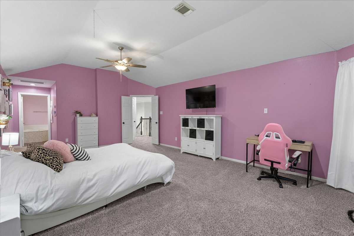 Spacious upstairs primary bedroom with vibrant pink walls, featuring a cozy bed, modern ceiling fan, and a dedicated workspace with a stylish desk and chair.
