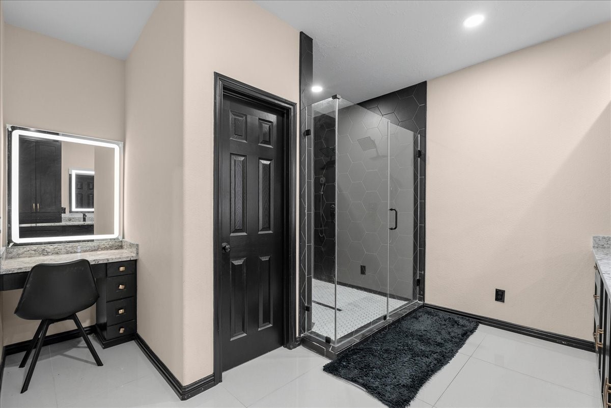 Elegant primary bathroom featuring a sleek glass-enclosed shower with modern hexagonal tiles and a stylish vanity area complete with a backlit mirror.