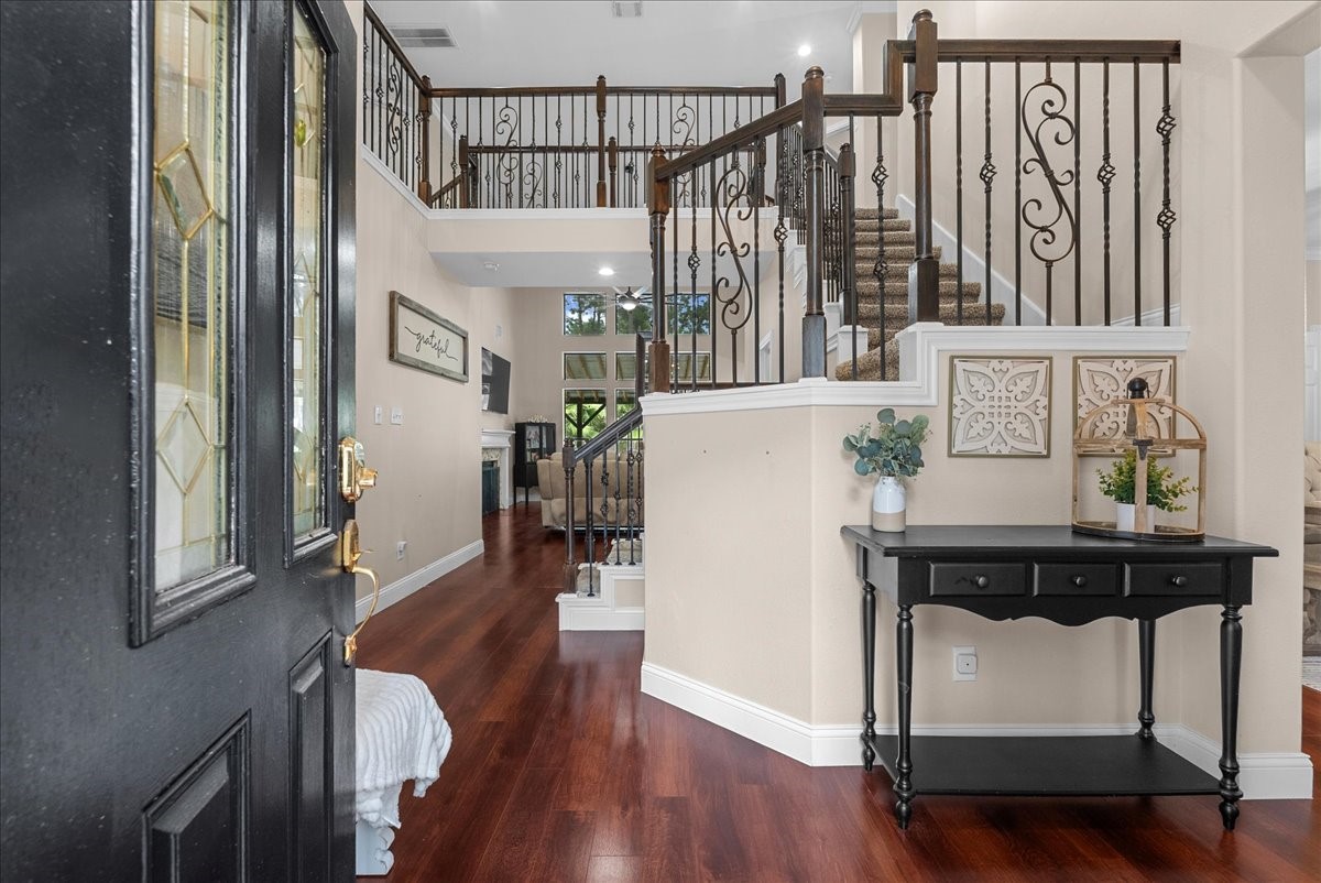 Elegant entryway featuring rich hardwood like floors and a charming staircase with decorative wrought iron railings, leading to a spacious and inviting living area.