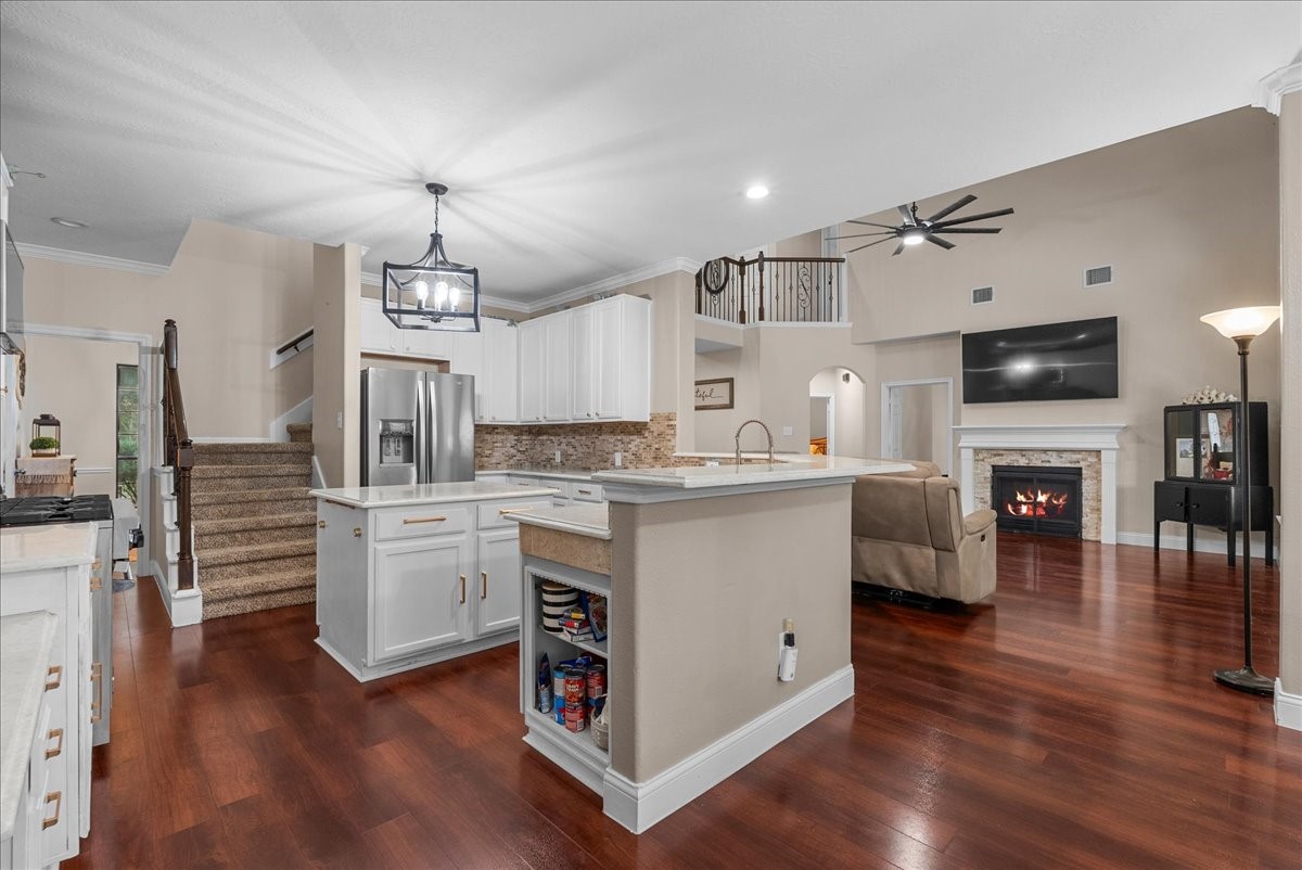 Spacious open-concept living area featuring a modern kitchen with stainless steel appliances, elegant cabinetry, and a large island. The cozy living room boasts a stylish fireplace and high ceilings, enhanced by natural light and wood like flooring.