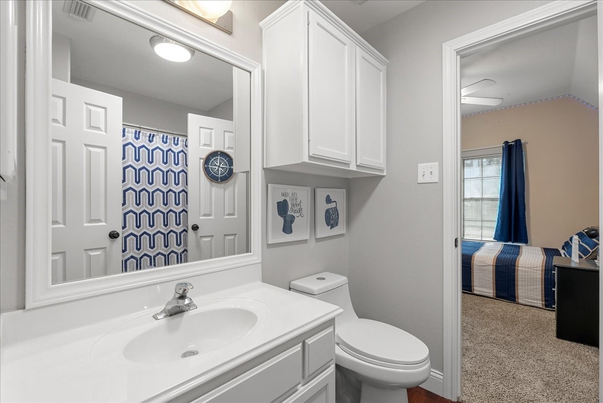 Bright bathroom with modern fixtures, ample storage, and a stylish blue geometric shower curtain, leading into a cozy bedroom with natural light.