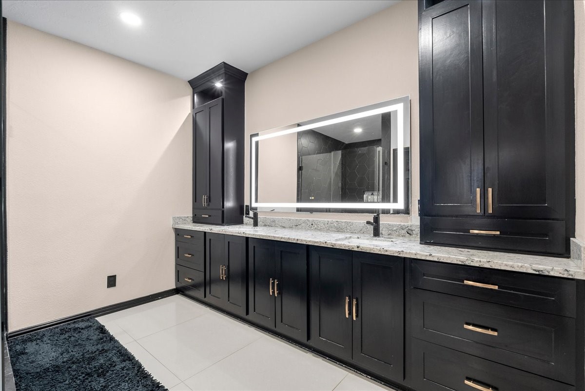 Elegant primary bathroom featuring sleek black cabinetry, a spacious dual-sink vanity with a granite countertop, and a modern backlit mirror.