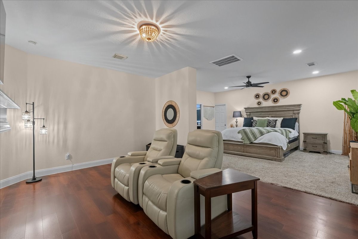 Spacious bedroom suite featuring a cozy seating area with plush recliners, elegant hardwood like floors, and a stylishly bed, creating a perfect retreat.