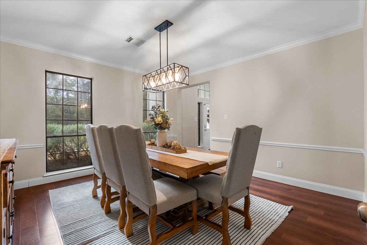 Elegant dining room with rich wood like floring, a large window offering natural light, and a stylish chandelier above a spacious table, perfect for gatherings.
