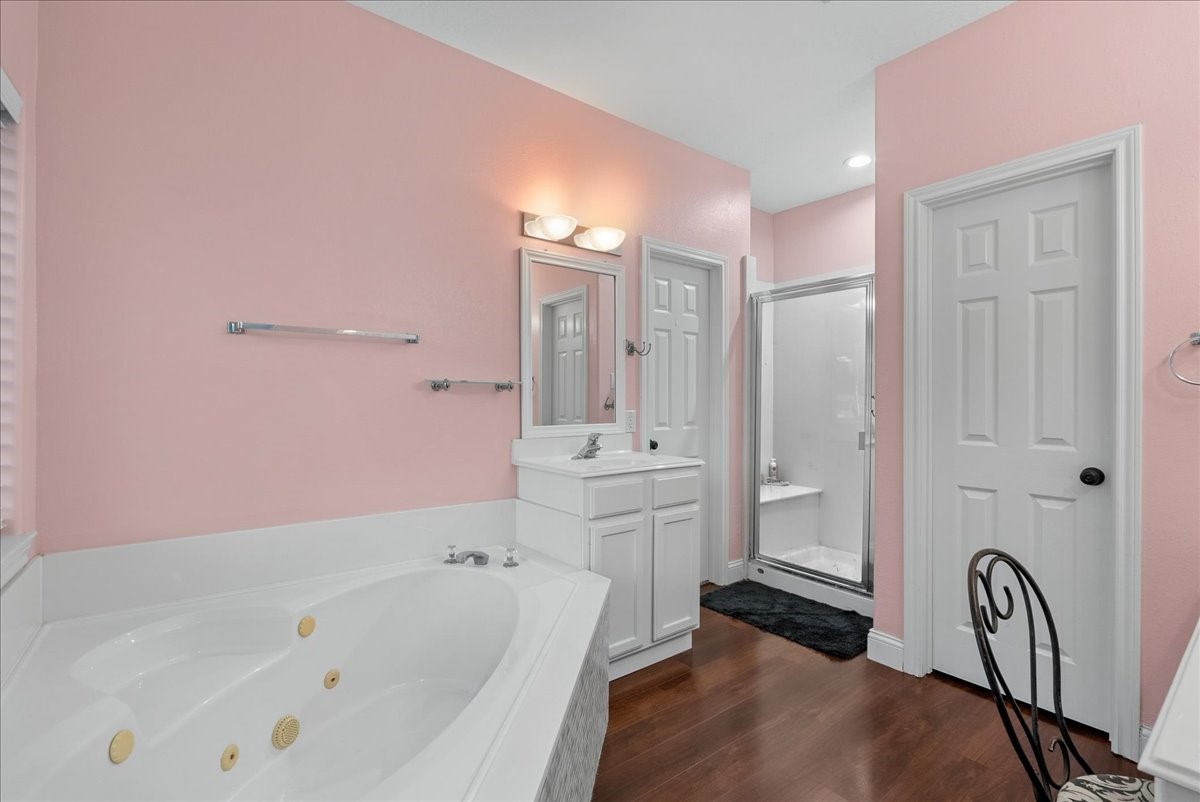 Charming bathroom with soft pink walls, featuring a luxurious jetted tub, a sleek walk-in shower, and elegant wood like flooring.
