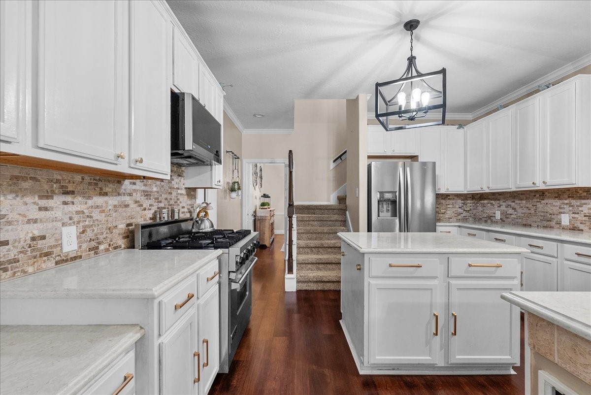 Spacious kitchen featuring elegant white cabinetry, sleek stainless steel appliances, and a charming brick backsplash, complemented by rich wood like flooring and a stylish central island.