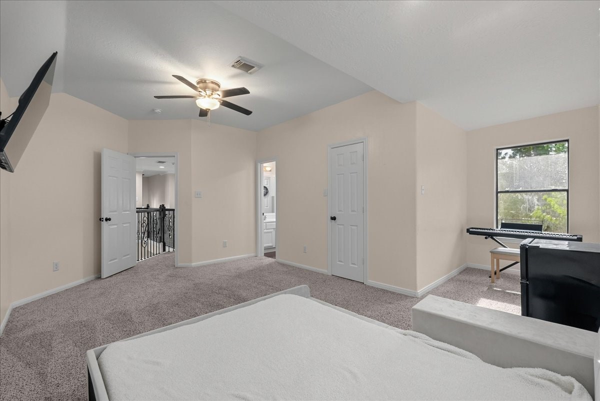 Spacious bedroom with plush carpeting, featuring a ceiling fan, large window for natural light, and convenient access to an en-suite bathroom and hallway.