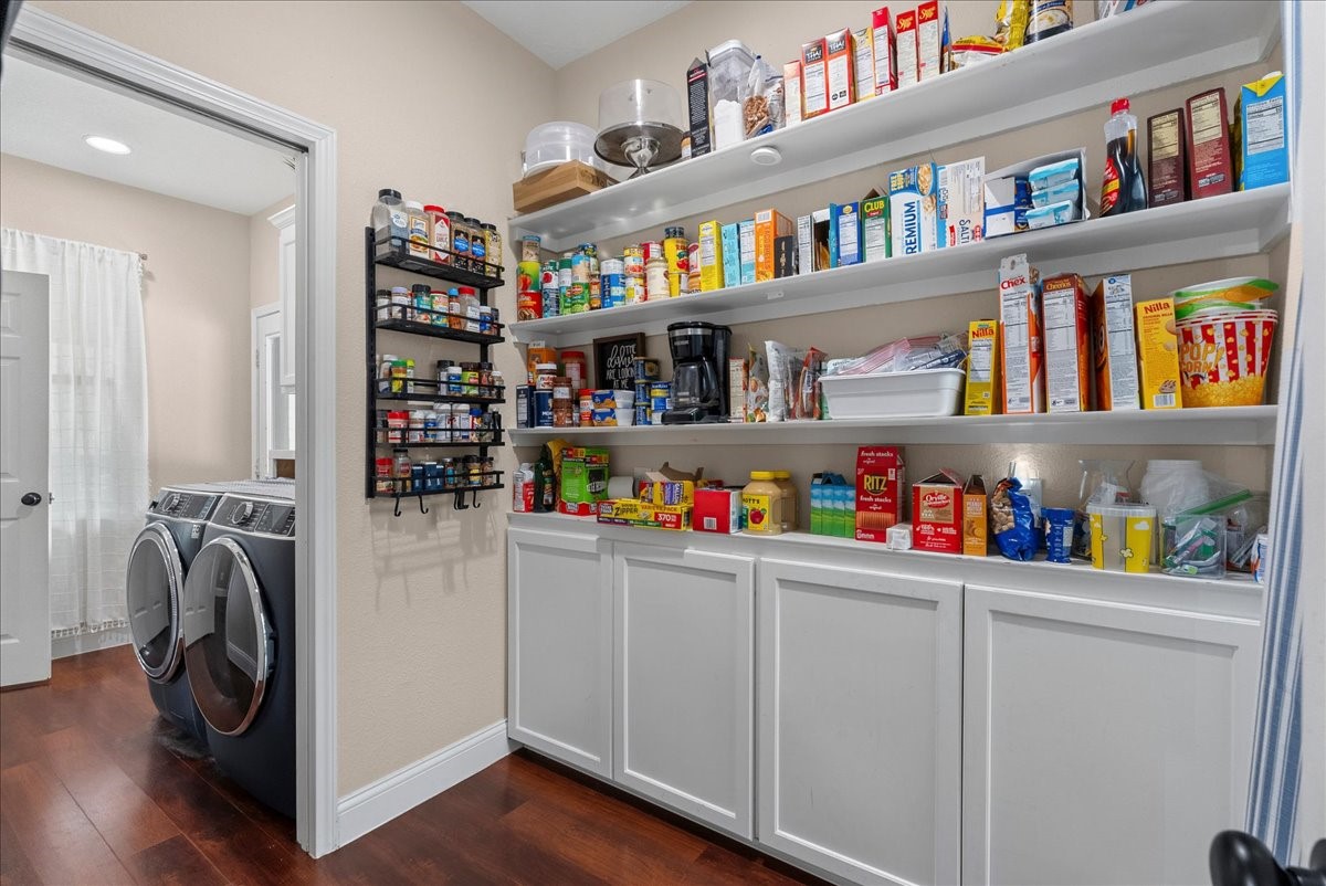 Spacious pantry with ample shelving for organized storage, adjacent to a modern laundry area with sleek appliances and hardwood like flooring.