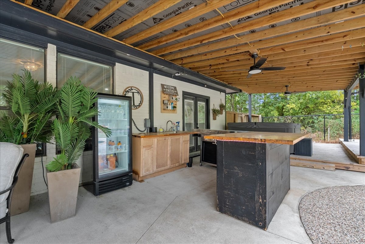 Spacious covered patio featuring a modern outdoor kitchen with a sleek bar, mini-fridge, and hot tub, perfect for entertaining and relaxation.