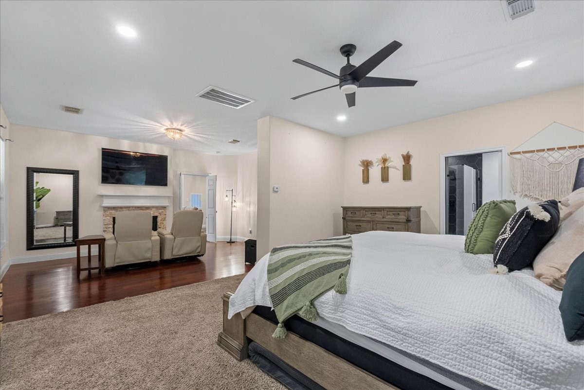 Spacious primary bedroom featuring elegant hardwood like floors, a cozy seating area by the fireplace, and modern ceiling fan, creating a luxurious retreat.