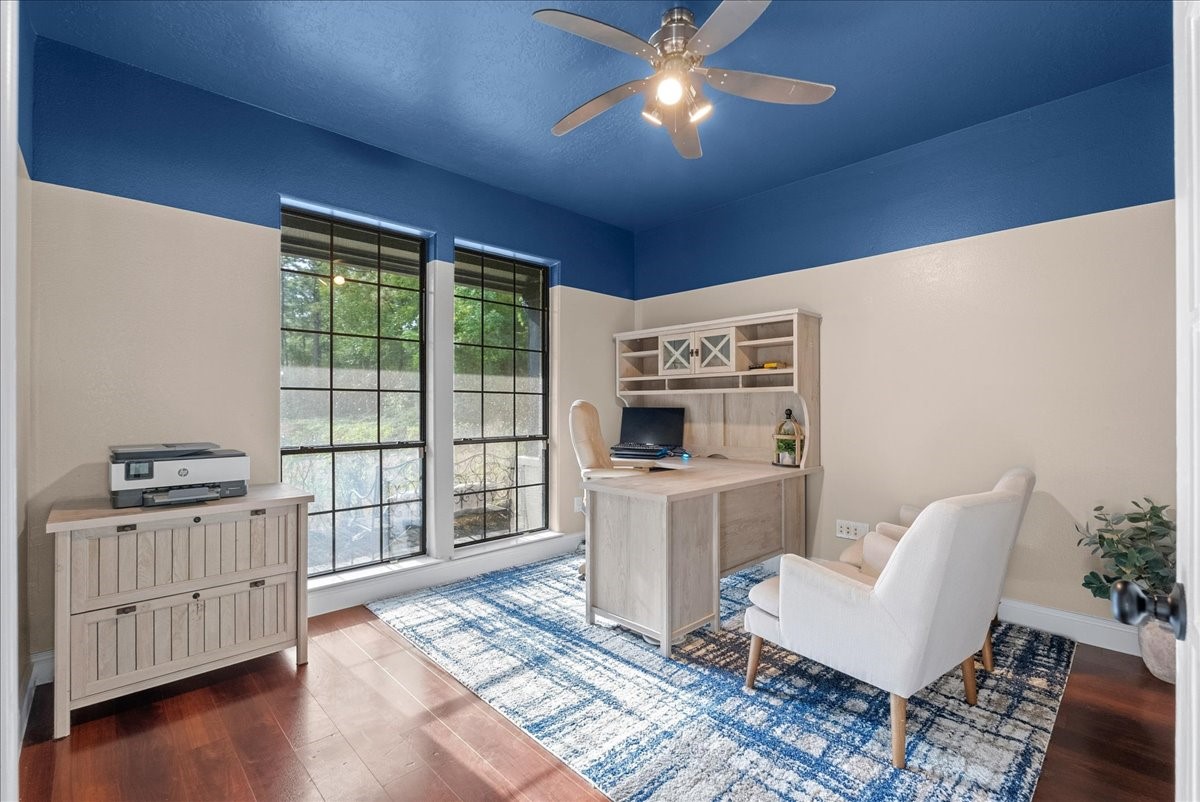 Bright home office with large windows, modern ceiling fan, and stylish furniture, offering a productive and comfortable workspace.