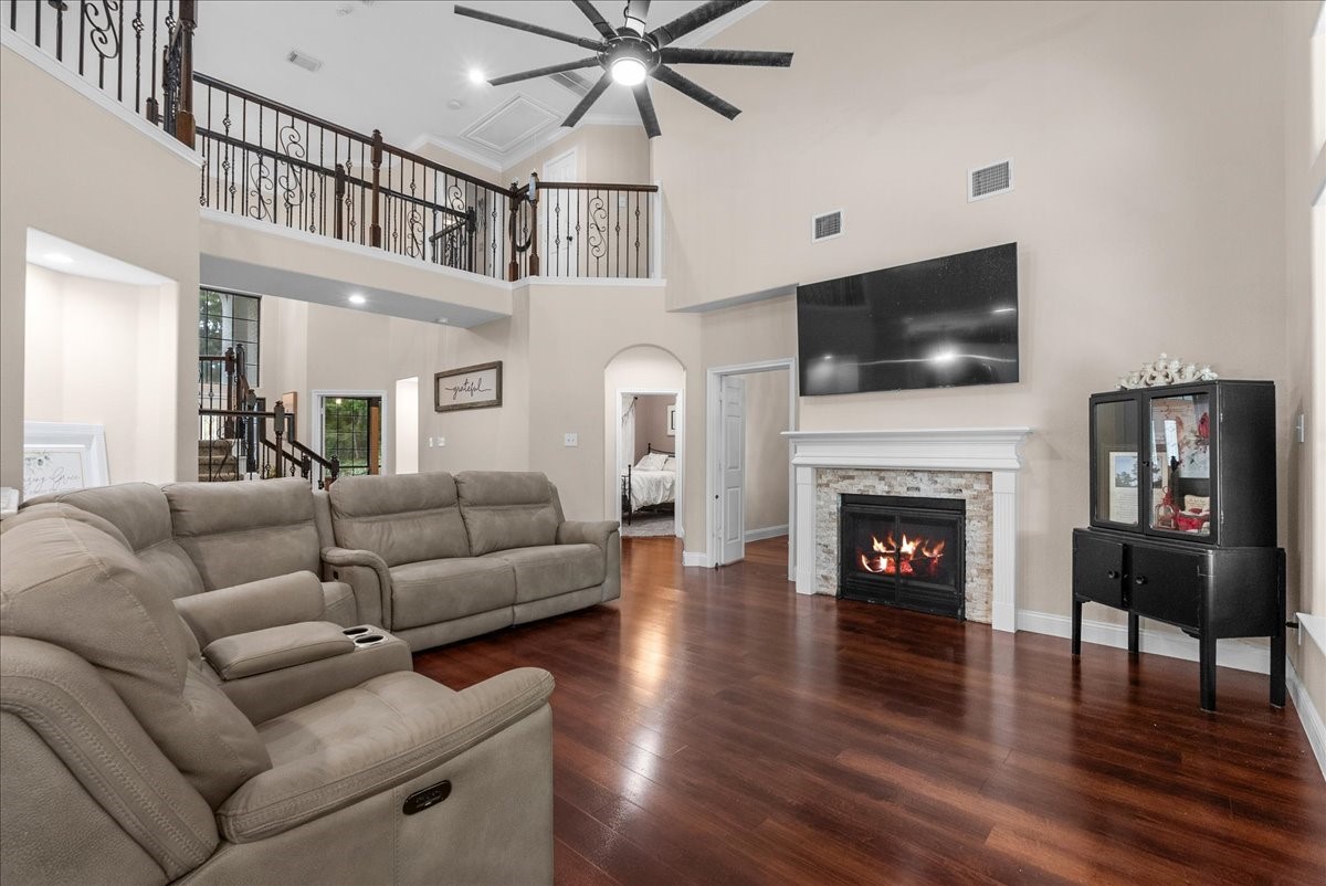 Spacious living room featuring high ceilings, a cozy fireplace, and a modern staircase, complemented by elegant wood like flooring and a abundance of natural light.
