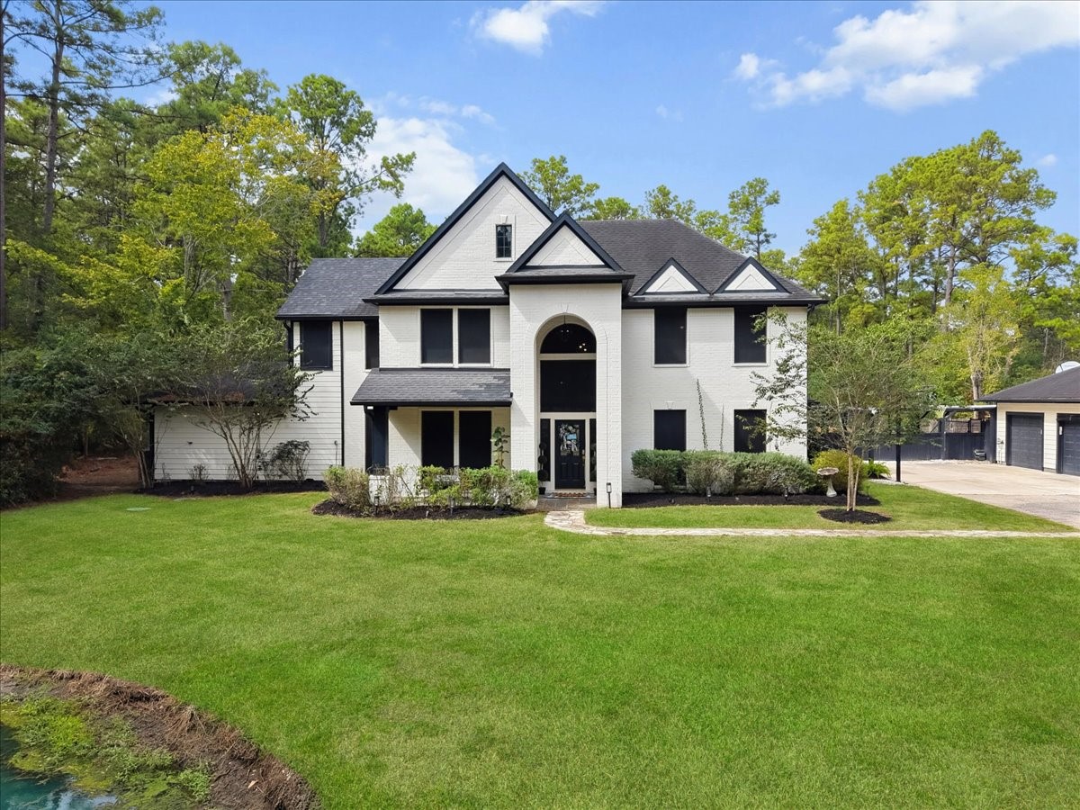 Elegant two-story home with a striking black and white faade, surrounded by lush greenery and nestled in a serene, wooded setting.
