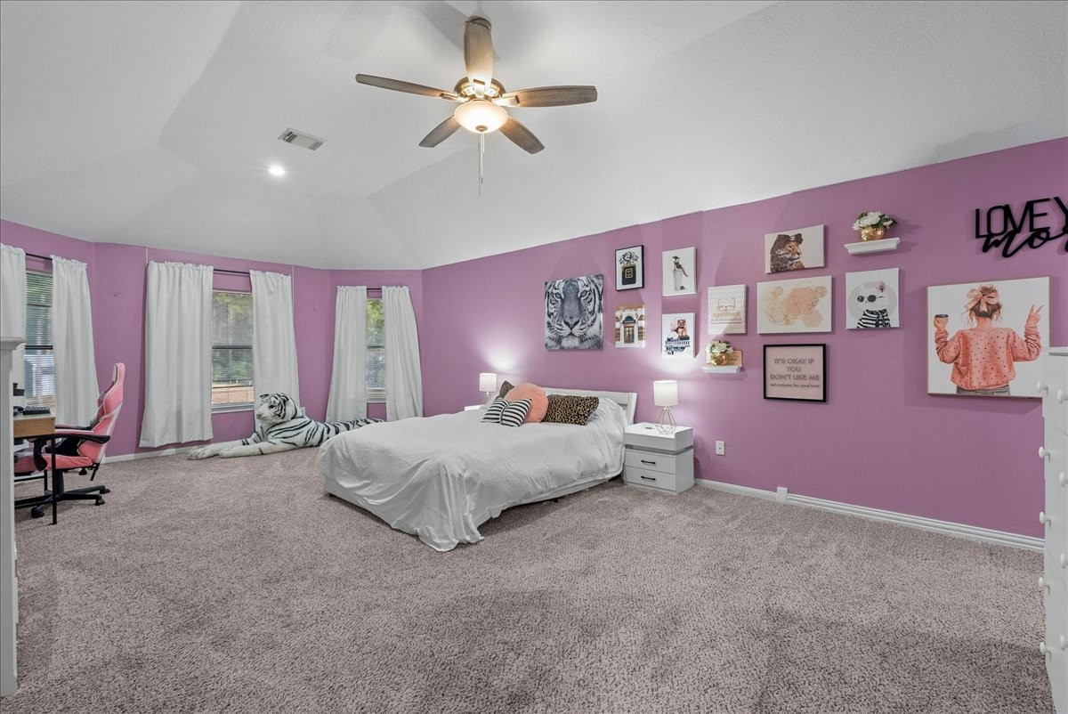 Spacious upstairs primary bedroom with vibrant pink walls, cozy carpeting, and a stylish gallery wall, featuring a comfortable bed and ample natural light.