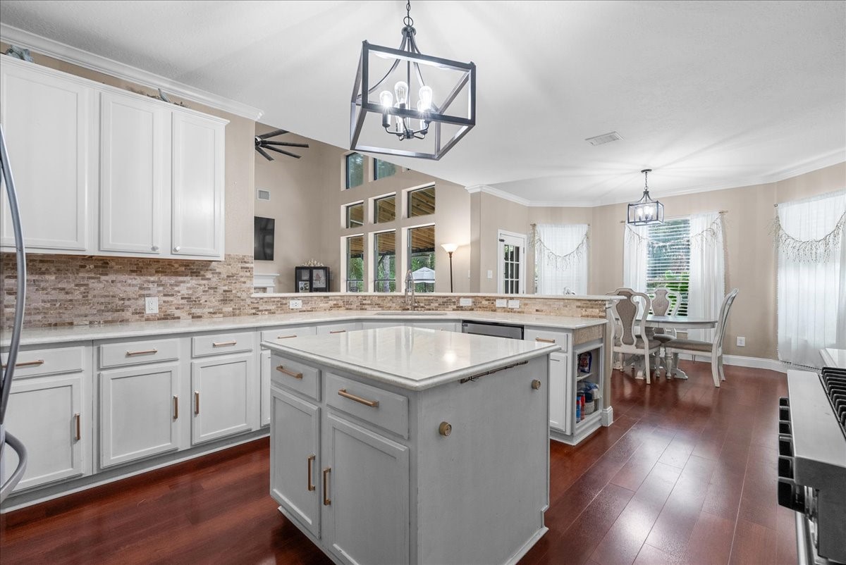 Bright and inviting kitchen features elegant white cabinetry, a spacious island with modern lighting fixtures, and an open layout leading to a cozy dining area with large windows.