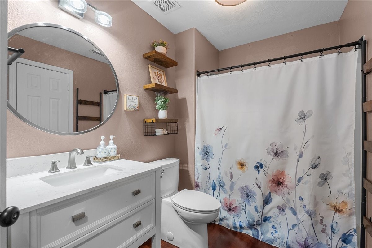 Charming bathroom featuring a stylish round mirror, elegant vanity, and a floral shower curtain that adds a touch of color and warmth.