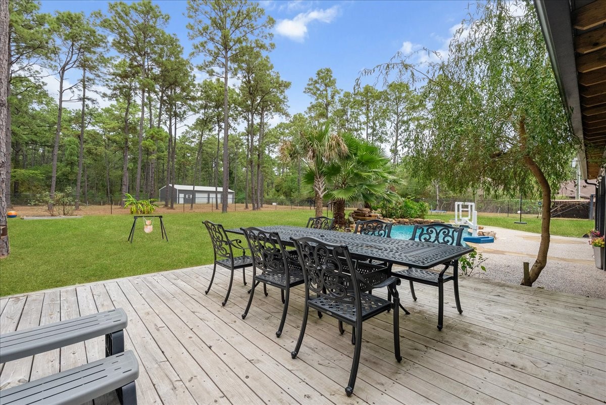 Expansive backyard retreat featuring a spacious deck with elegant wrought iron furniture, a lush lawn, and a sparkling pool surrounded by mature trees for added privacy and tranquility.