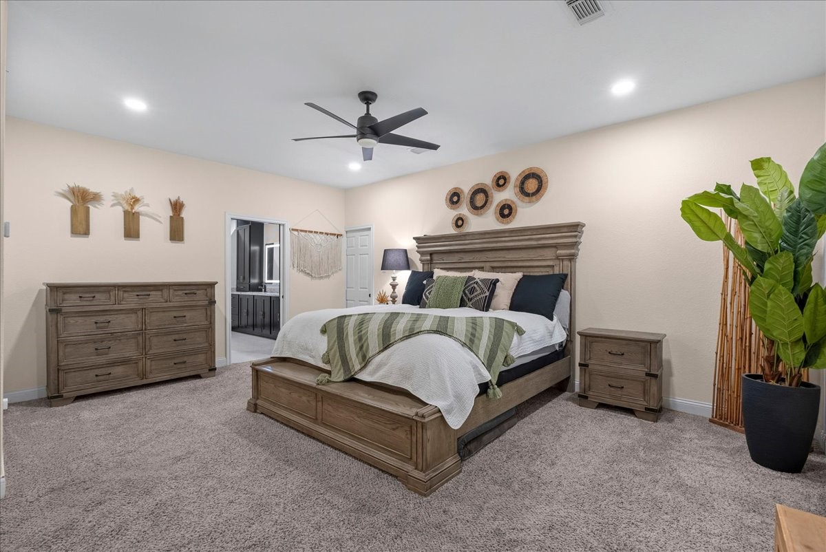 Spacious primary bedroom with a plush carpet, featuring a stylish wooden bed frame and matching dresser. The room is accented by modern wall decor, a ceiling fan, and abundant natural light, creating a cozy and inviting atmosphere.