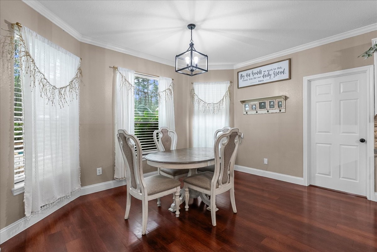 Charming dining area with elegant hardwood like floors, a stylish round table, and abundant natural light streaming through large windows adorned with sheer curtains.