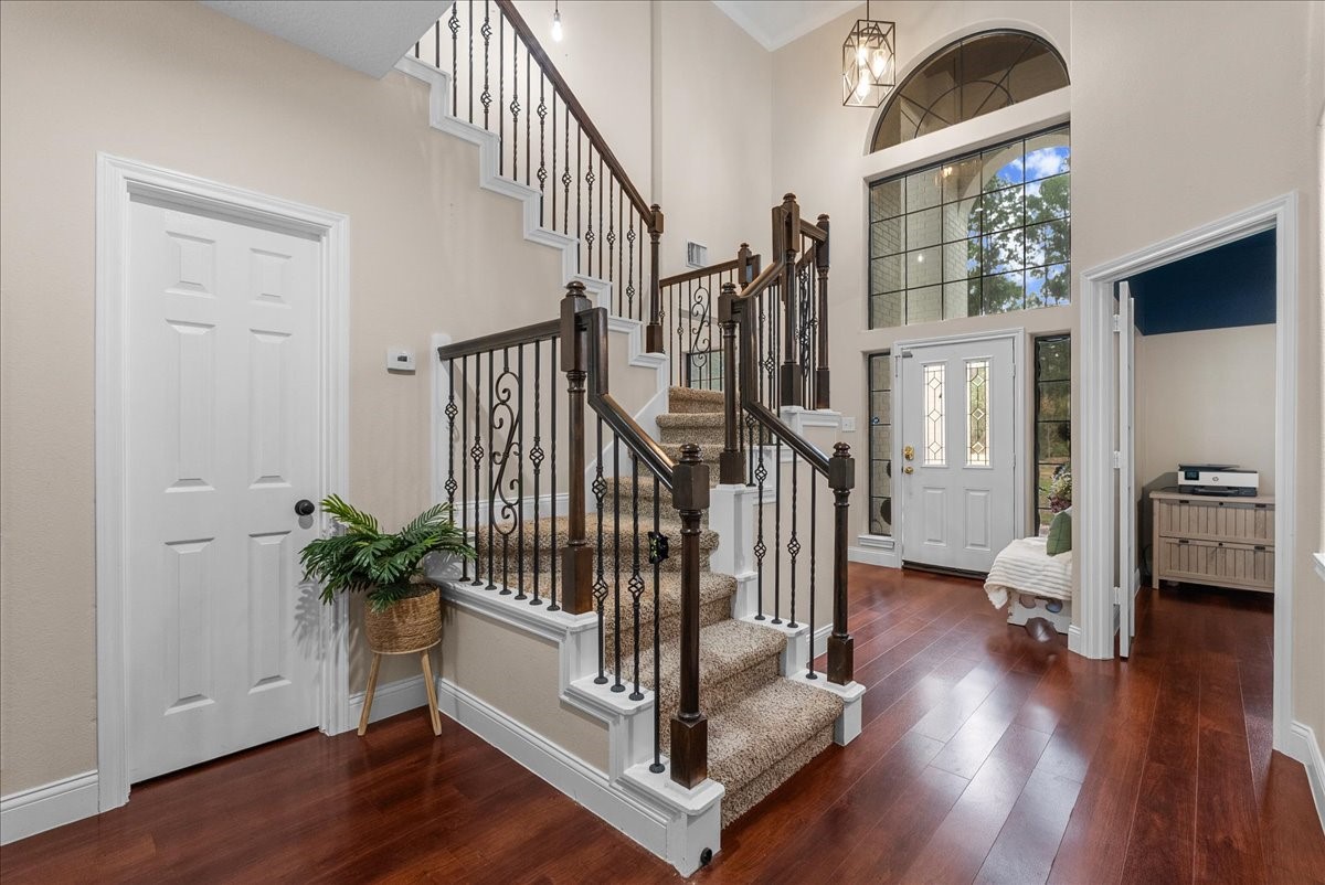 Elegant foyer with a grand staircase, featuring wrought iron railings and rich hardwood like floors, complemented by high ceilings and a large arched window for natural light.