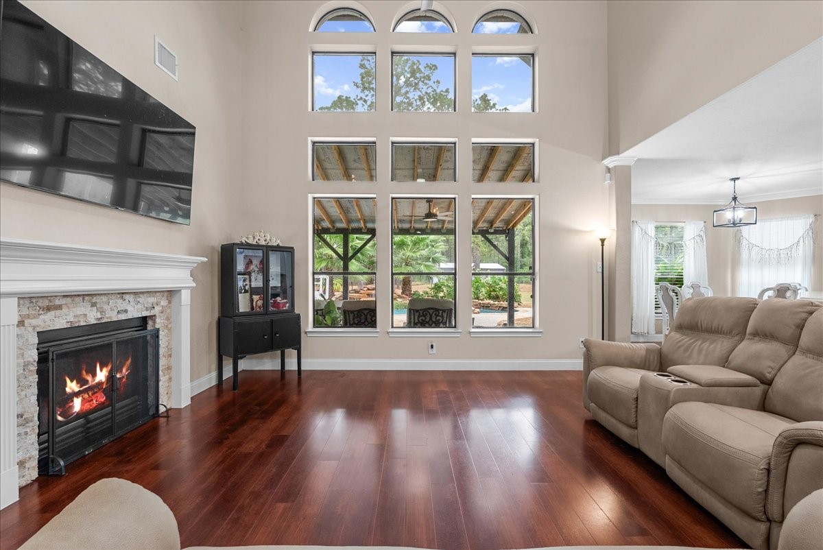 Stunning living room with soaring ceilings and expansive windows, featuring a cozy fireplace and elegant hardwood like floors, seamlessly flowing into the dining area for a perfect blend of comfort and style.