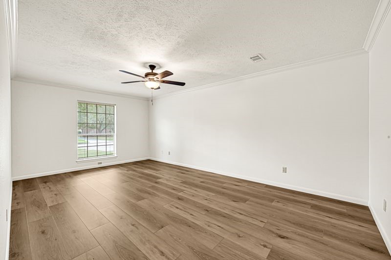 Spacious room with elegant wood flooring, a large window for natural light, and a ceiling fan for comfort.