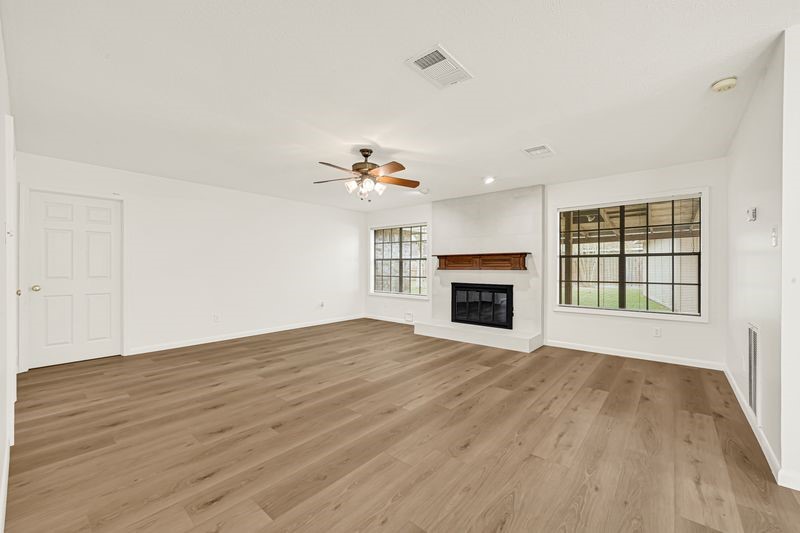 Spacious living room with elegant wood flooring, a cozy fireplace, and large windows offering abundant natural light.