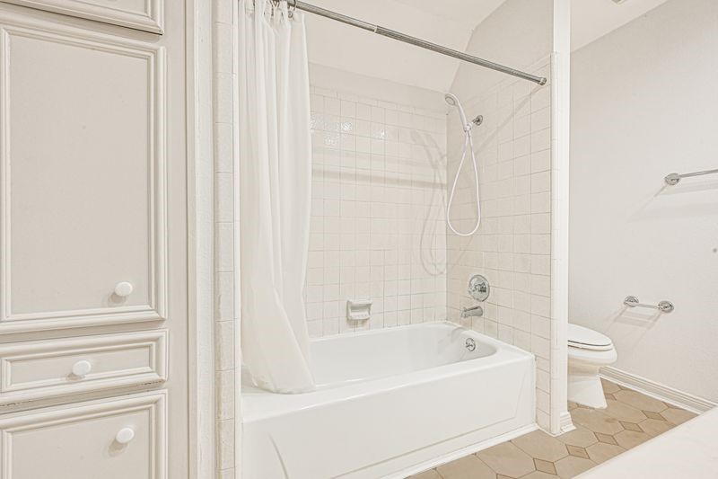 Bright and inviting bathroom featuring a classic tile shower-tub combo, ample storage with cabinetry, and a neutral palette for a serene atmosphere.