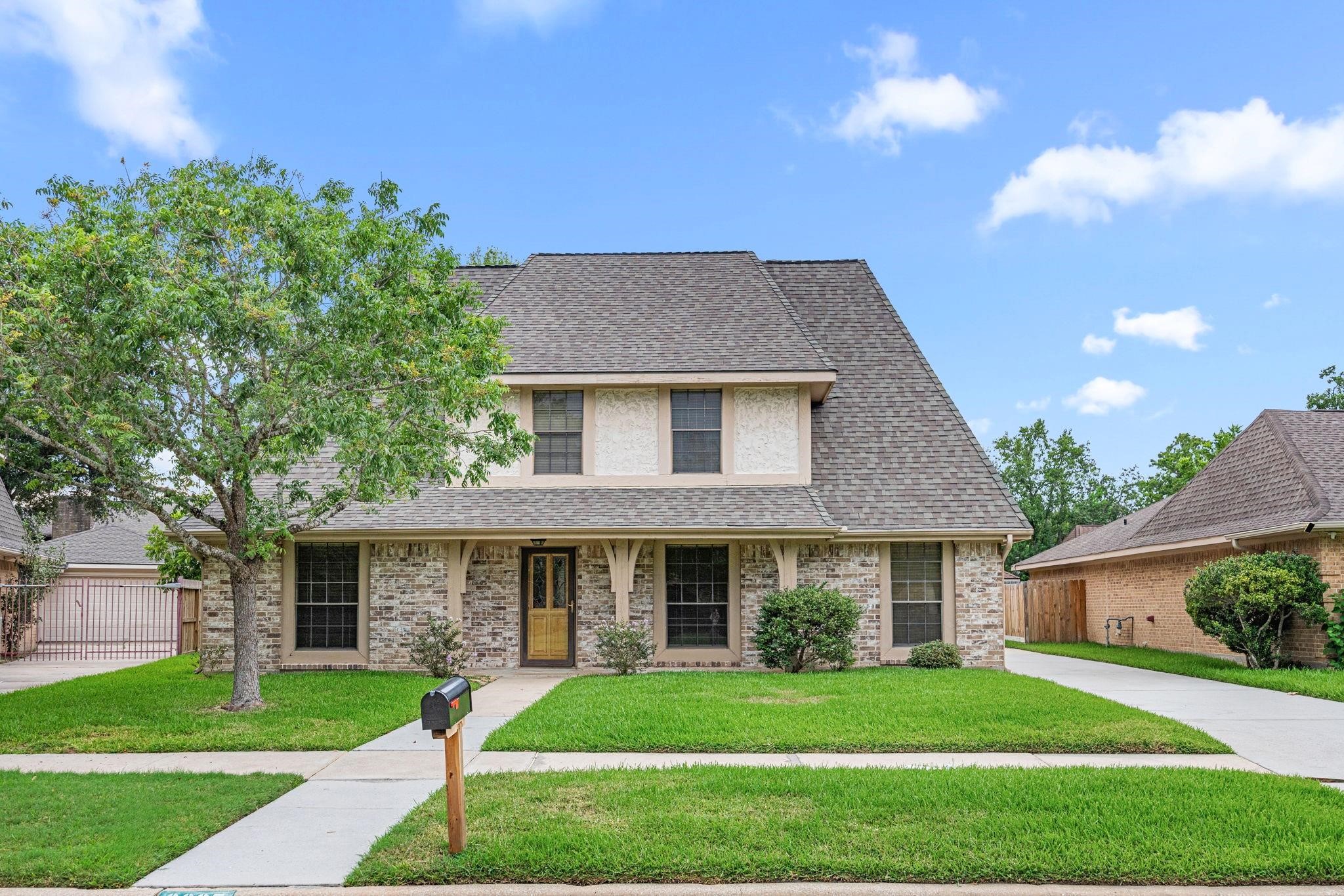 Charming two-story home with a classic brick facade, inviting covered porch, and a spacious front yard, perfect for family living.