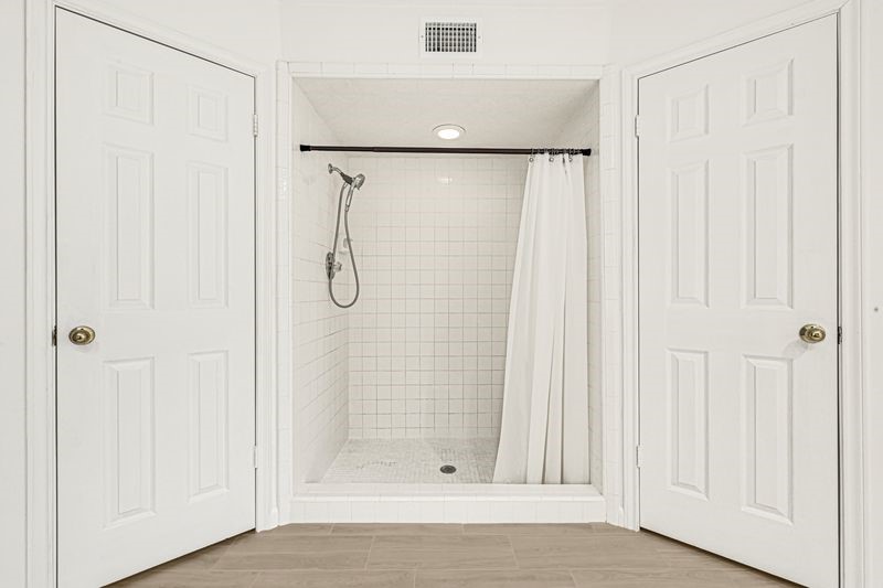 Spacious walk-in shower with sleek white tiles and a convenient handheld showerhead, flanked by double doors for easy access.