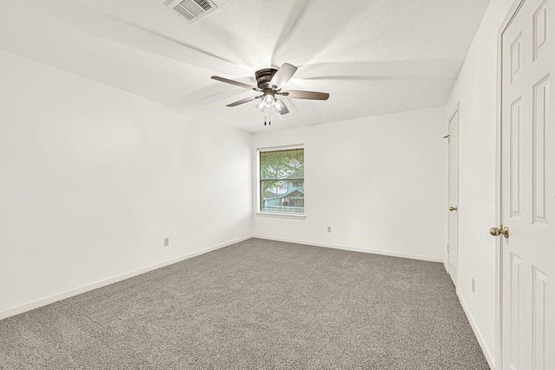 Spacious bedroom featuring plush carpeting, a ceiling fan for comfort, and ample natural light from a large window.