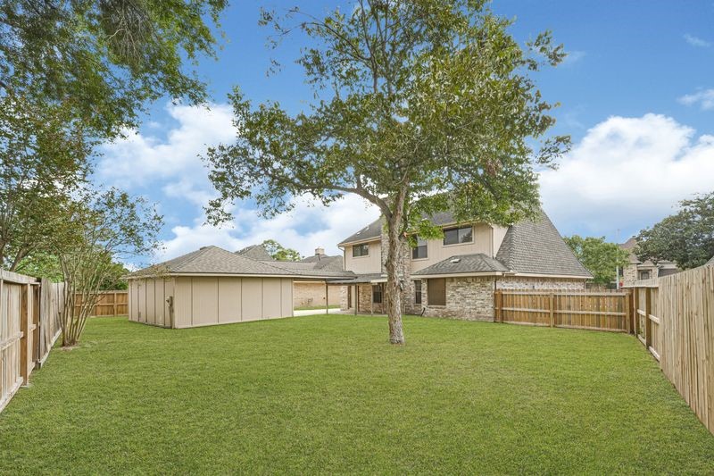 Spacious backyard with lush green lawn, mature trees, and a privacy fence, perfect for outdoor activities and relaxation.