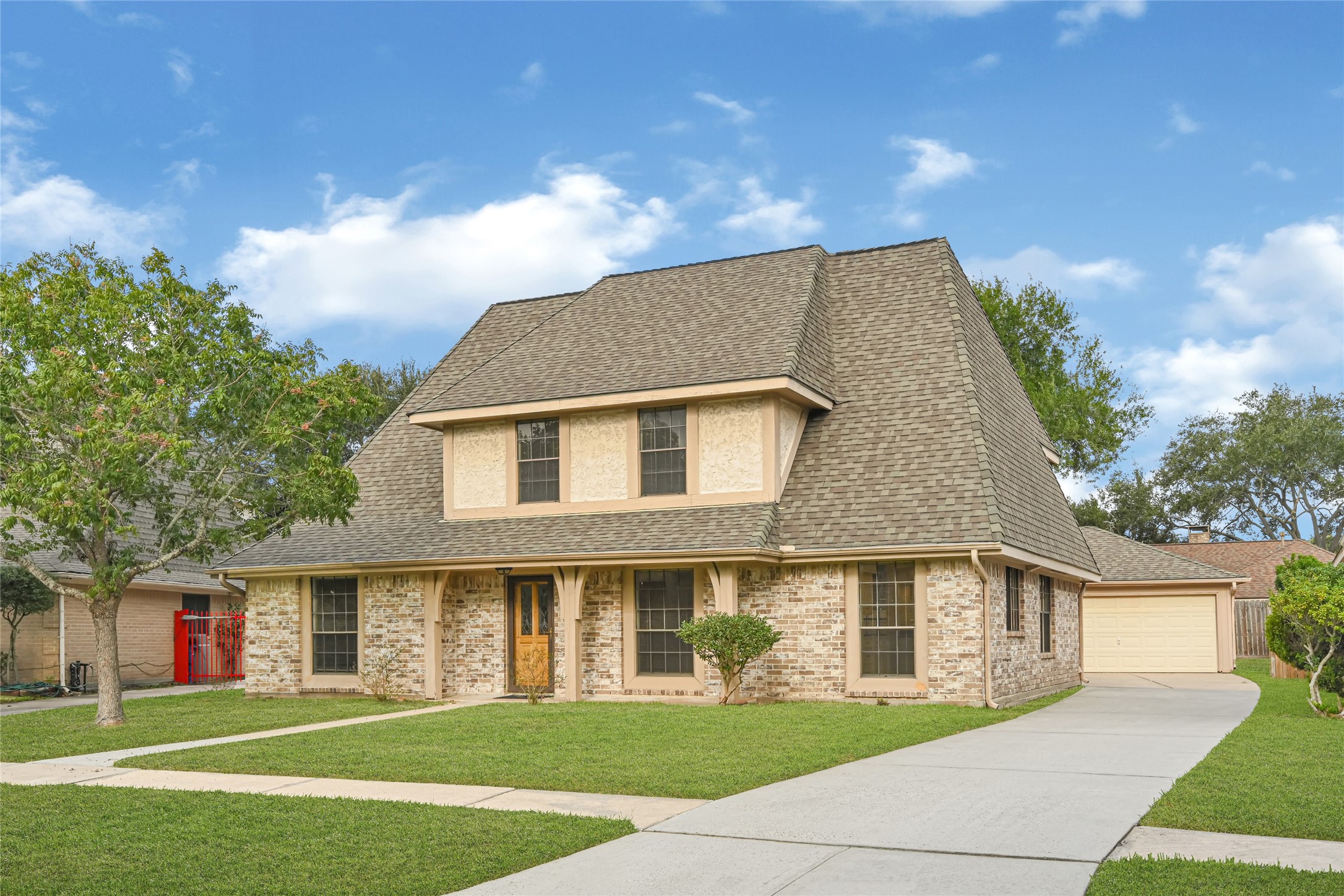 Charming two-story brick home with a steeply pitched roof, spacious driveway, and well-maintained front lawn, offering a welcoming and picturesque curb appeal.