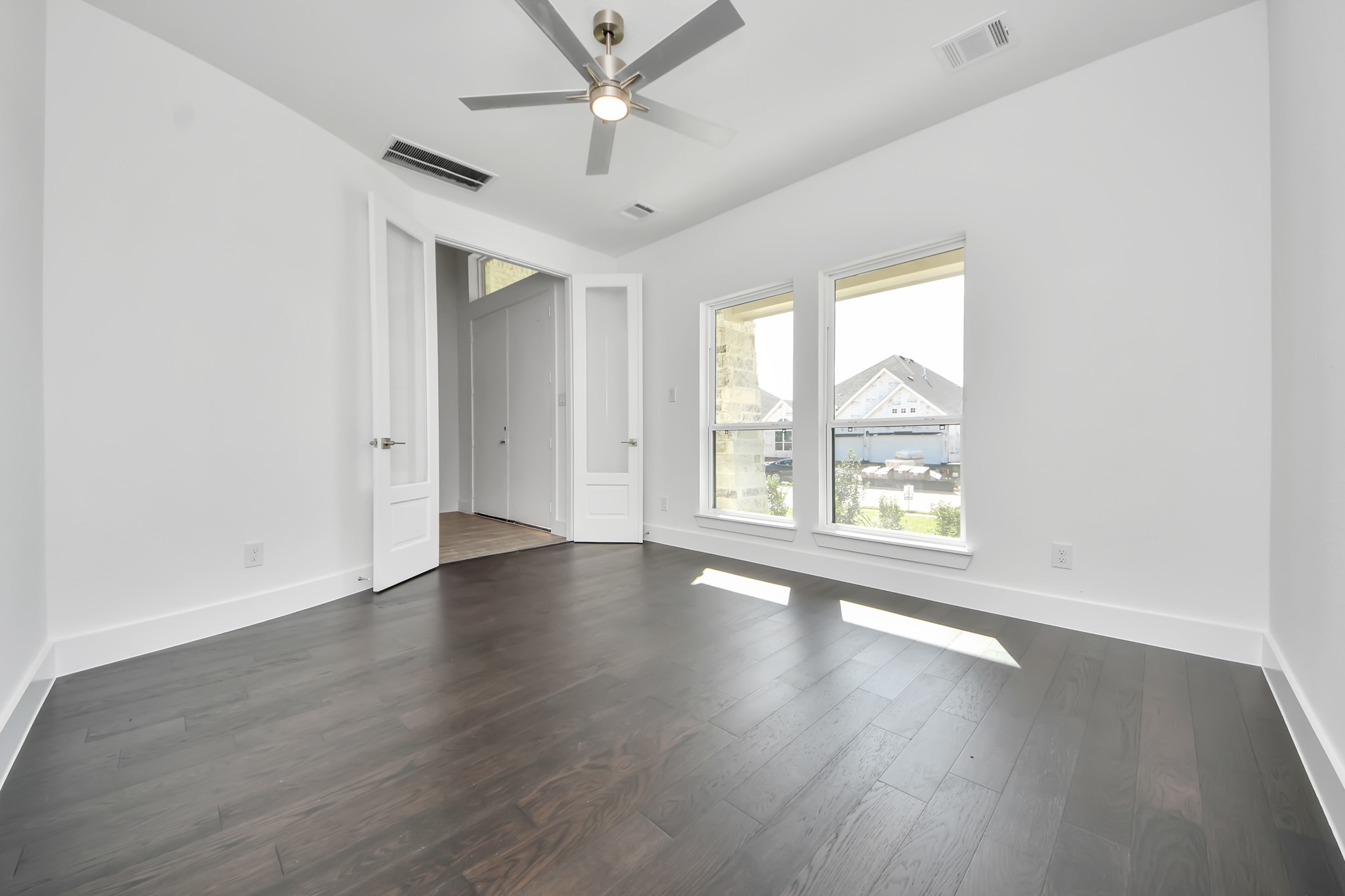 Experience the perfect blend of sophistication and warmth in this home office, boasting elegant wood-look tile flooring and flooded with natural light from expansive windows and French doors.
